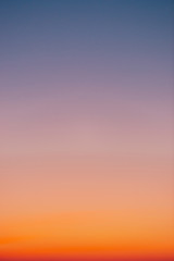Predawn clear sky with orange horizon and violet atmosphere. Smooth orange violet gradient of dawn sky. Background of day beginning. Heaven at early morning with copy space. Sunset, sunrise backdrop
