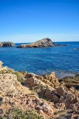 Fototapeta na wymiar Blue water envelop a dark grey rock or islet, that just rise above the surface along the southern coast of Spain 
