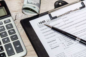 tax forms 1040, dollars, calculator, pen and magnifier on gray, wooden table