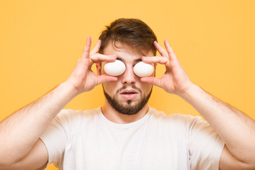 Man stands on a yellow background and holds eggs at the level of the eye. Eggs in front of a man isolated on a yellow background.