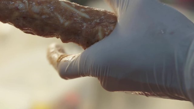 Hands of chef in white rubber gloves making kebab close up. Cook forming shape of raw uncooked minced meat on skewer. Traditional food preparation in restaurant. Georgian cuisine