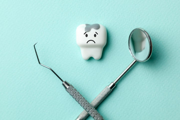 White tooth with caries is sad on green mint background  and dentist tools mirror, hook.