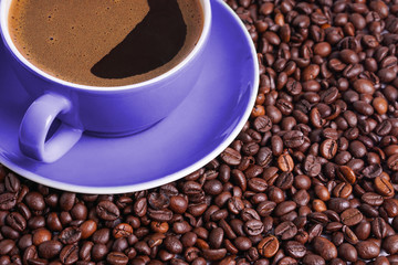 Coffee in purple cup on table surrounded with coffee beans