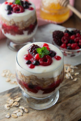 Glass jar withovernight oats, granola and yogurt with berry, raspberries and blackberries on wooden cutting board over wooden background. Healthy food.