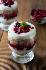Glass jar withovernight oats, granola and yogurt with berry, raspberries and blackberries on wooden cutting board over wooden background. Healthy food.