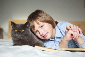 Adorable kid boy and british shorthair  cat lying together on the bed at home
