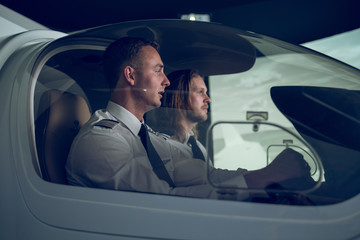 Side view of pilot with male trainee flying in flight simulator