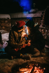 Nice couple in colored hats sitting near the fire.