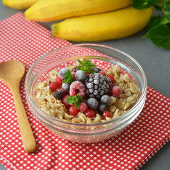 Healthy breakfast in a bowl with oatmeals, frozen berries, fresh strawberries, mint. Oat porridge with fruits. Square image.
