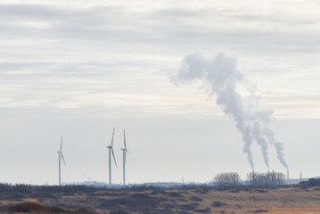 Smoking chimneys against which stands a wind power plant