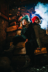 The guy and the girl are sitting on wooden beams and exhale blue smoke.