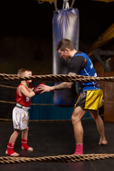 Trainer teaching a kid how to hit punches. Kid wearing boxing gloves and head guard training with his coach inside a boxing ring