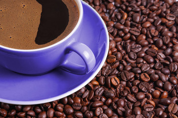 Coffee in purple cup on table surrounded with coffee beans