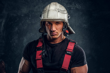 Studio portrait of a handsome man wearing a fire helmet and gloves, looking at a camera