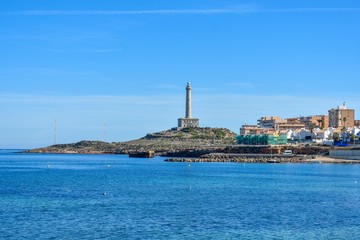 The lighthouse of Cabo de Palos sitting on-top of a hill, surrounded by the blue water of the Mediterranean
