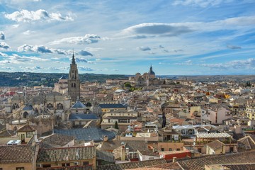 Fototapeta na wymiar A tiled rooftop view of Toledo, Spain with the towers of the cathedral and monastery peaking out from amongst the closely spaced buildings. 