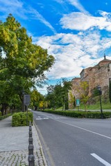 A broad modern road lined with trees on the one side and the ancient defensive walls of Toledo, Spain on the other