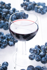 glass of red wine and blue grapes on white wooden table background