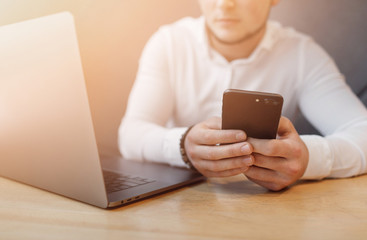 Man's hands using smart phone and laptop in interior.