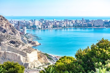 The view from the fort of Alicante, Spain, showing the city below, with the blue water of the Mediterranean in the bay below and on the far-side of the city.