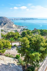 The view from the fort of Alicante, Spain, showing the city below, with the blue water of the Mediterranean in the bay below and on the far-side of the city.