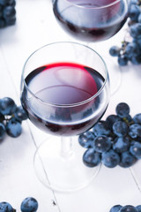 two glasses of red wine and blue grapes on white wooden table background