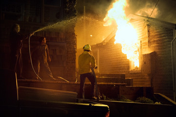 Two individuals extinguishing a house on fire.