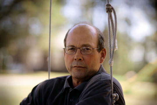 Close up of a mature man sitting on the swing in the park.