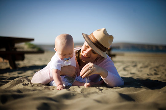 Mother and her young baby playing in sand at the beach.