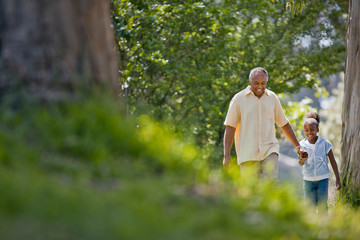Happy senior man walking hand in hand with his young granddaughter through a park.