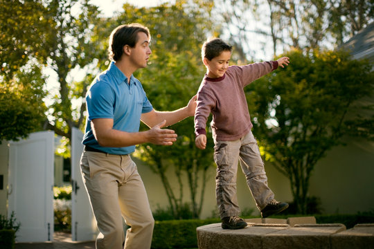 Happy mid adult man helping his son to balance on a stone wall.