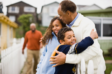 Grandfather hugging his Granddaughter and Grandson with their Father in the background