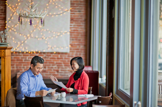 Two smiling mature colleagues discuss a business deal over coffee in a local cafe.