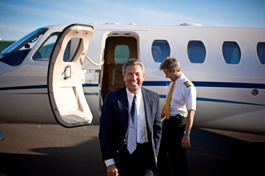 A businessman and a pilot standing in front of a private jet and smiling