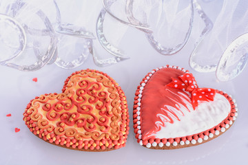 A pair of beautiful homemade gingerbreads for a wedding celebration or Valentine's day on a white glass background next to bridal veil, closeup