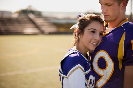 Cheerleader snuggled into football player's chest.