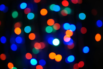 Multi-color blue holiday garland. Garland is blurred. Many big colorful round lights. Fully defocused photo. Blurred background and foreground. Holiday mood. New Year and Christmas is coming.
