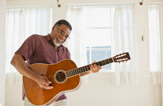 Smiling man playing acoustic guitar at home