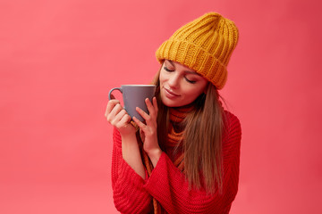 Beautiful teenage girl in warm cozy sweater with cup of hot drink. Red background. Studio