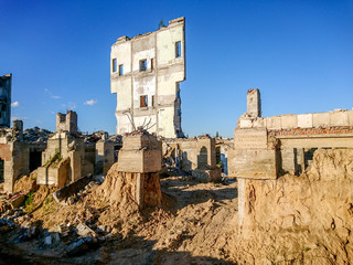 The ruins of a large destroyed building, pieces of stone, concrete, clay and metal against the blue clear sky.