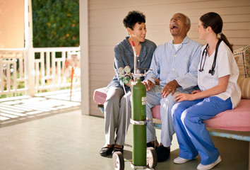 Senior man with nasal tubing sitting on the deck of rest-home and laughing with his wife and nurse.