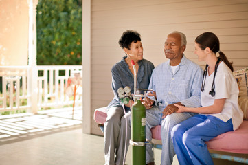 Senior man with nasal tubing sitting on the deck of rest-home with his wife and nurse.