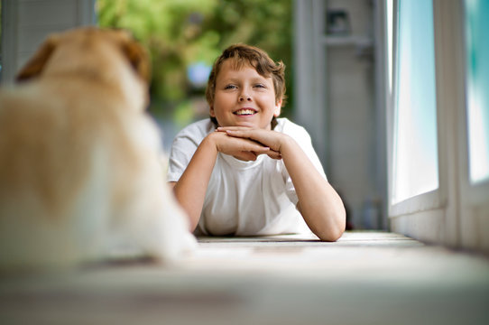 Smiling teenage boy daydreaming while lying down on a hardwood floor with his dog.
