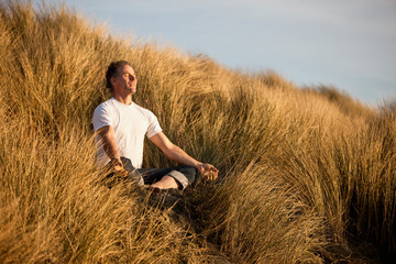 Mature man meditating while sitting cross-legged on the sand dune.