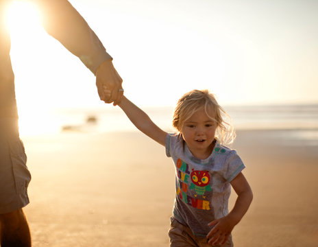 Small girl holding her father's hand at the beach.