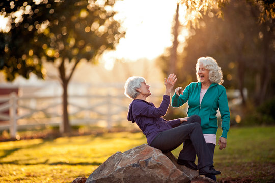 Two smiling senior women giving each other a high-five in a park.