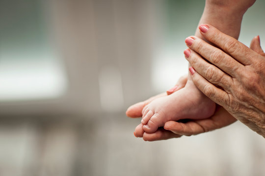 Close-up of elderly woman's hands as she holds her baby grandson's foot.