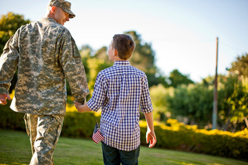 Rear view of male soldier with his son walking in backyard
