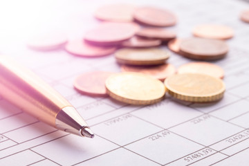 Stack of euro euro coins on old black wooden table. Pen and accounting documents with numbers