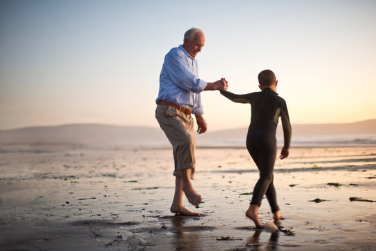 Smiling senior man holding hands with his grandson at the beach.